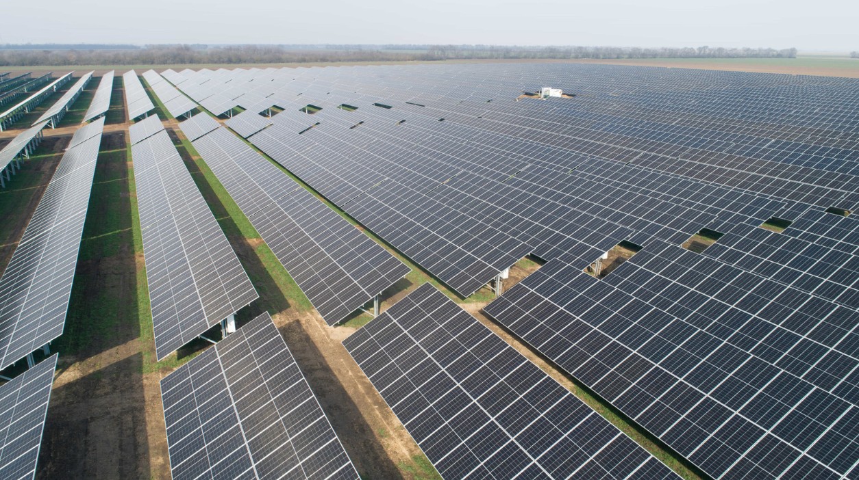 Weitläufige Luftaufnahme eines riesigen Solarparks, der ein großes Feld mit Reihen von Photovoltaikmodulen bedeckt.