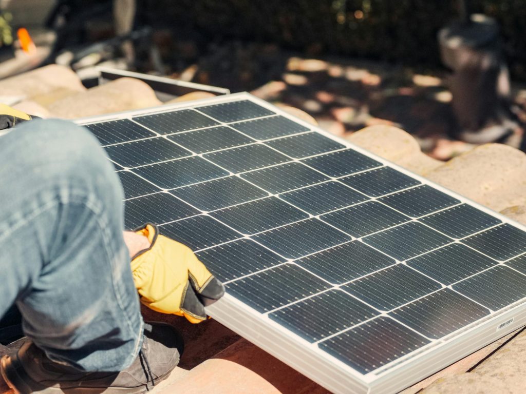 Ein Arbeiter installiert ein Solarpanel auf einem sonnenbeschienenen Dach und ist damit ein Beispiel für erneuerbare Energie.